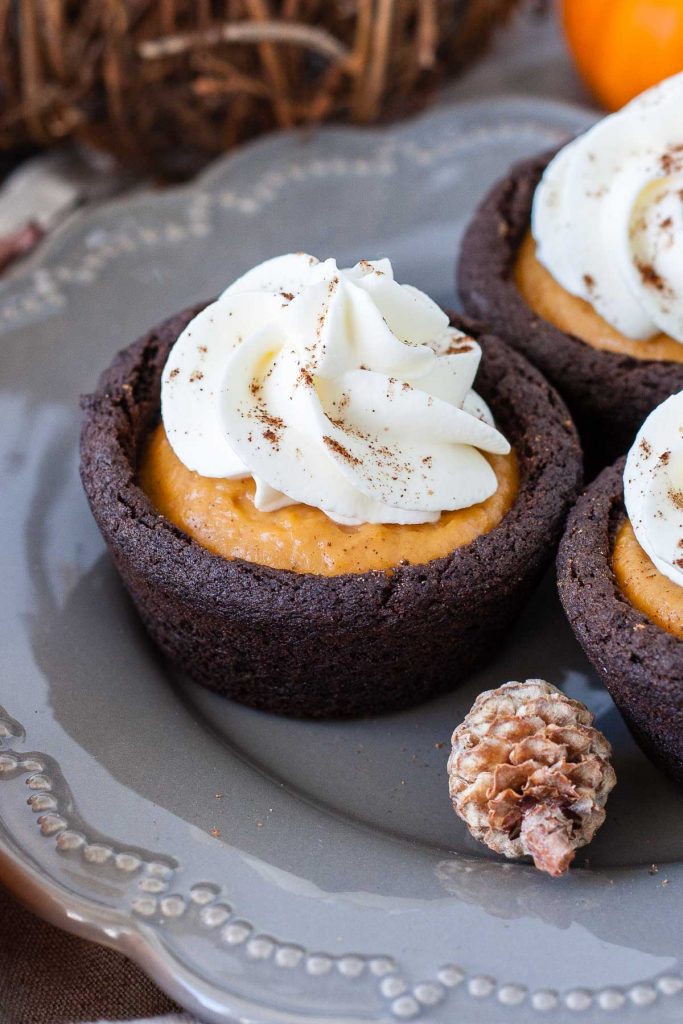 Chocolate pumpkin spice cookie cups filled with pumpkin pudding and topped with fresh whipped cream.
