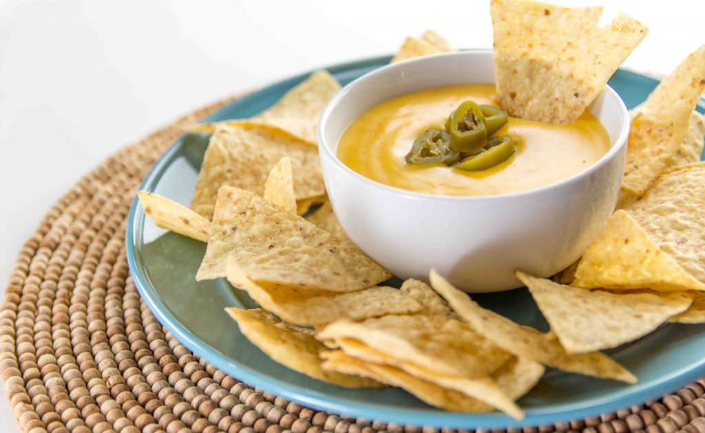 A plate of nacho chips and a bowl of nacho cheese 