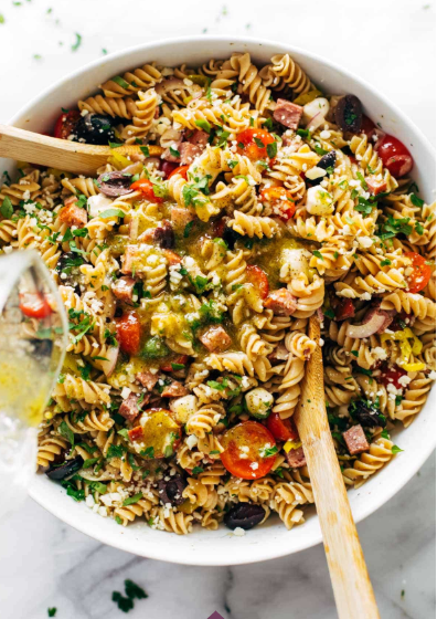 A bowl of Italian pasta salad with rotini, juicy tomatoes, fresh mozzarella, red onion, salami, olives, herbs, and a drench of quick homemade Italian dressing.