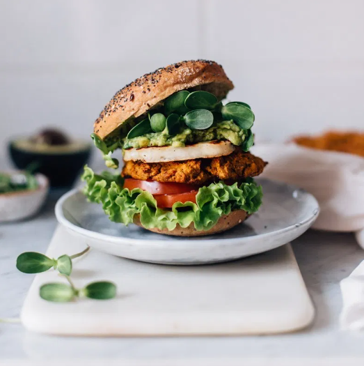 Sweet potato lentil burger with fried halloumi, leafy greens, tomato, mashed avocado, and sprouts
