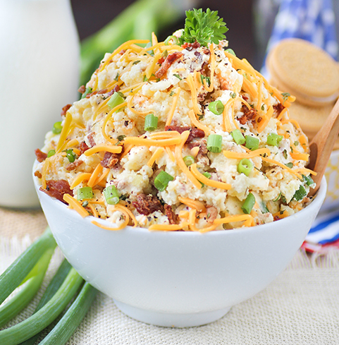 Loaded baked potato salad served cold with pieces of bacon, green onions, and cheddar cheese