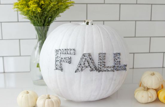 A pumpkin painted white decorated a string art that says Fall