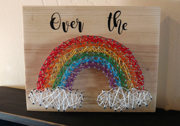A rainbow string art with a saying "Over the" on top of it.