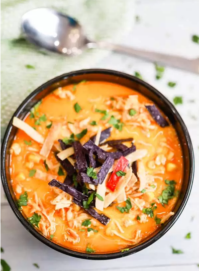 Slow cooker creamy chicken tortilla soup garnished with tortilla strips, more cheese and cilantro