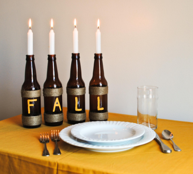4 brown glass bottles wrapped with twine and has a F A L L letter in each bottle and lighted candles plunked on them