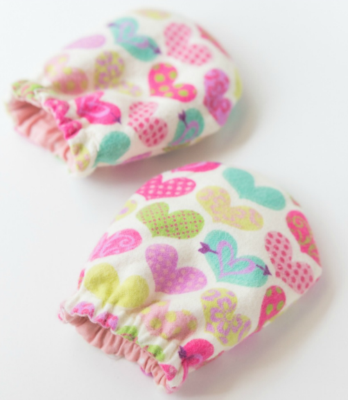 A pair of no scratch baby mittens with a different kinds of heart designs on it