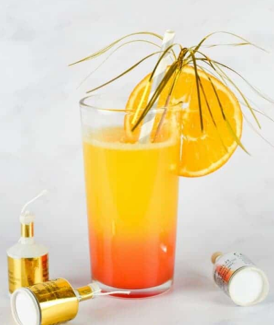 New Year sunrise mocktail on a glass with a sliced of orange and a straw and foil cocktail sticks.