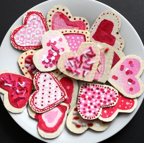 Valentines cookie made from cardboard painted red and pink with yarn sprinkles, pipe cleaners and paper confetti.