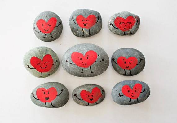 Different shape rocks painted red heart shape with different smiley faces on it using a fingerprint