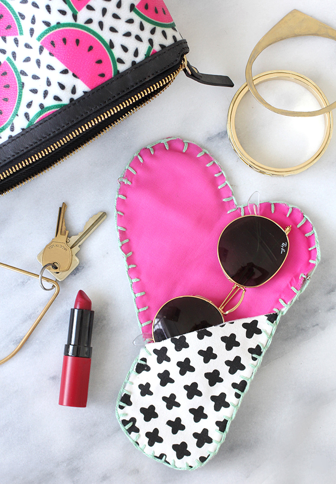 Heart shaped sunglasses case with a sunglasses on it, a coupe of key, a red lipstick and a watermelon designed pouch
