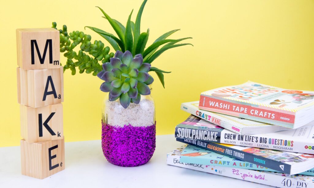 Diy glitter vase made from a mason jar covered half with purple glitter and a succulents plant coming out of the jar