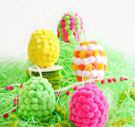 Plastic Easter eggs covered with colorful pompoms and a ribbon on top.