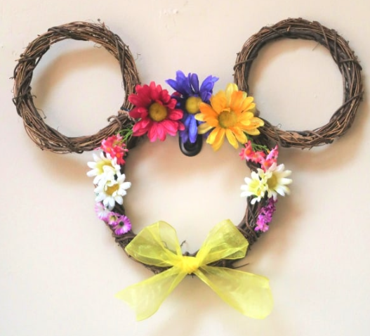 Mickey mouse shaped flower wreath with a different silk flowers on it and a yellow ribbon in the middle