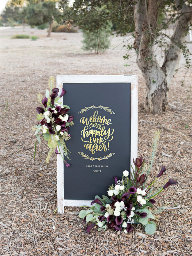 DIY wedding sign says welcome to our happily ever after Chad + Jacqueline 3.18.19 with flower arrangement on it