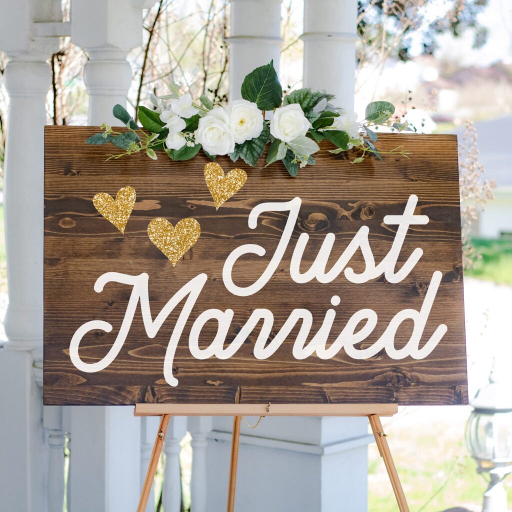 Gorgeous wedding sign says just married with three gold hearts on it and a white roses decorations above