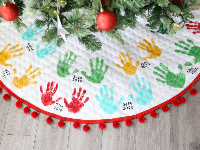 Handprint designed Christmas tree skirt with pom pom trim around the outer edge of the tree skirt.