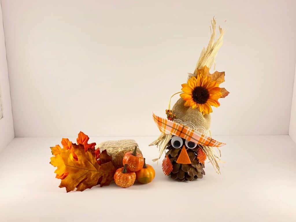 pine cone scarecrow with a checkered hat and flower decor for the fall season