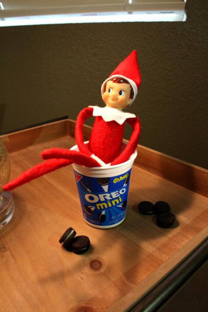 elf on the shelf sitting on a cup of oreo mini cookie