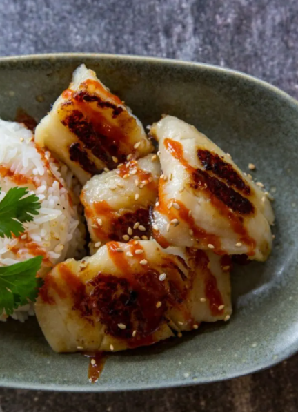 Miso Marinated Black Cod served over rice with a drizzle of soy sauce and sriracha