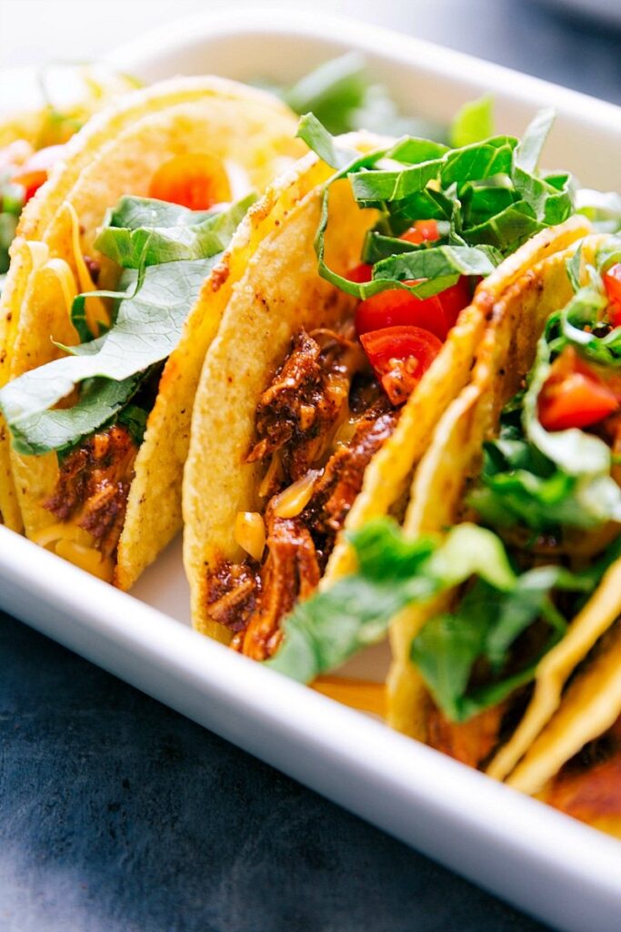 rotisserie chicken tacos topped with lettuce, and chopped cherry tomatoes