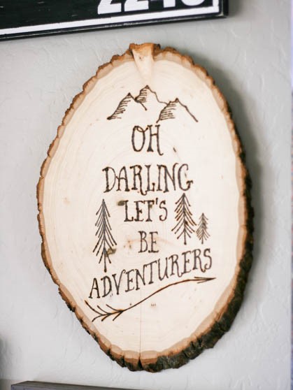 Wood burned wall art with mountains, trees, and text saying Oh Darling Let's Be Adventurers