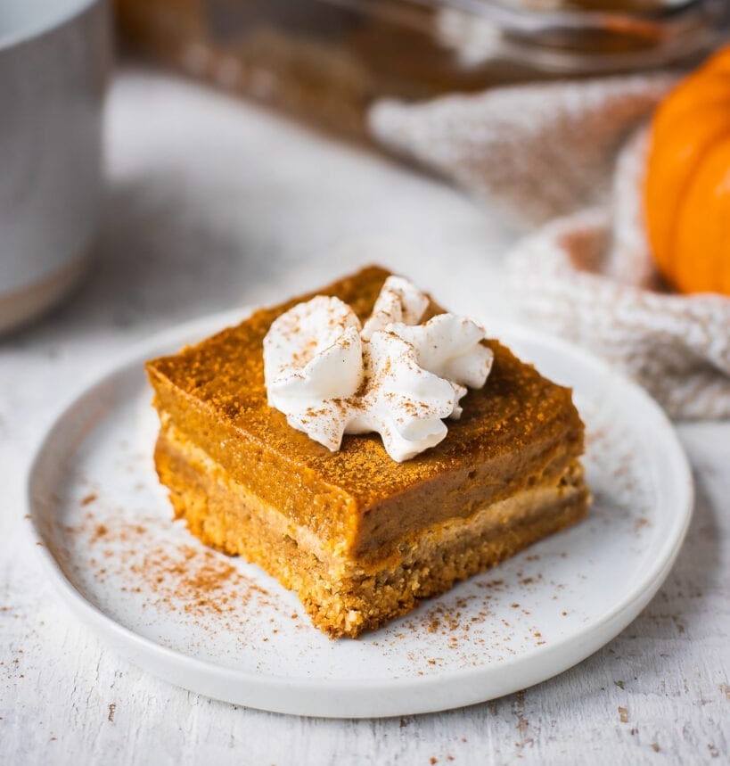 Pumpkin pie in bar form topped with whipped cream and sprinkled of spiced pecans