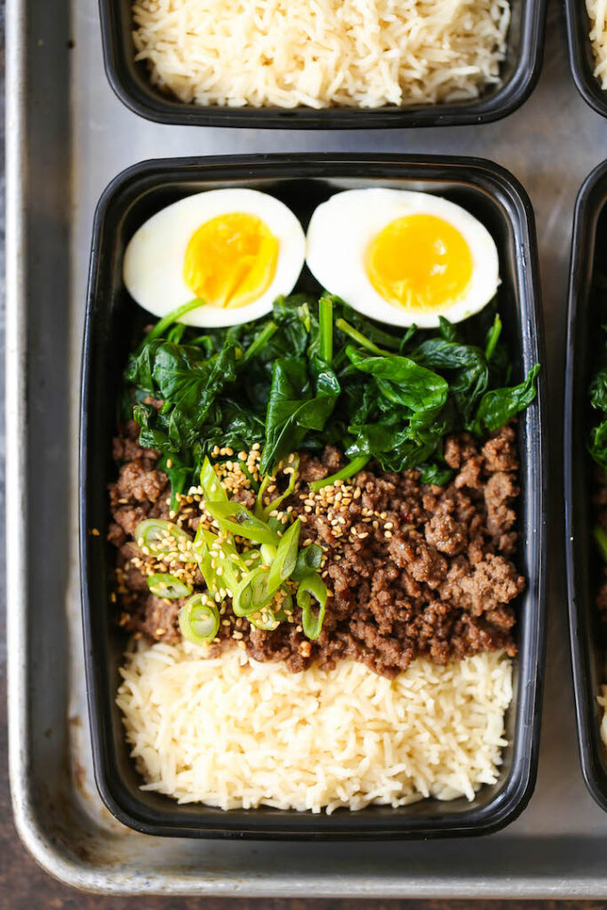 Korean beef bowl meal prep served with rice, eggs, spinach and garnished with green onion and sesame seeds