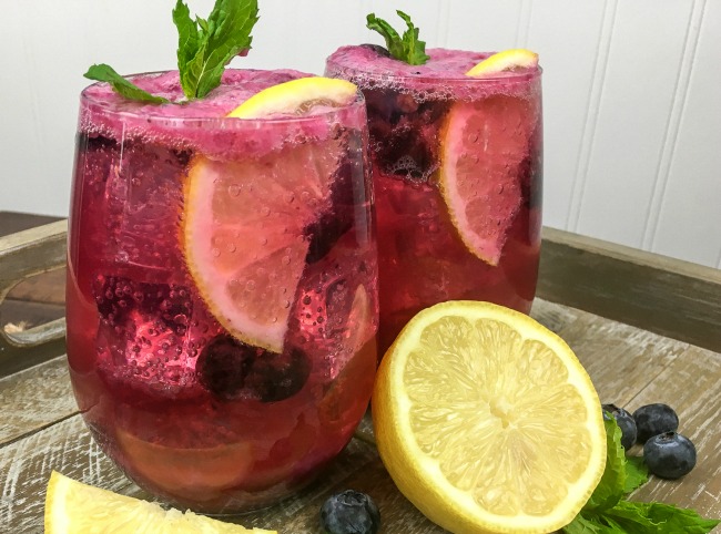 Sparkling Blueberry Maple Lemonade perfect for summer picnics garnish with sprigs of fresh mint, blueberries, and lemon wedges
