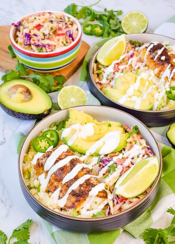 Low carb Fish Taco bowls topped with avocado slices, and drizzle with sauce